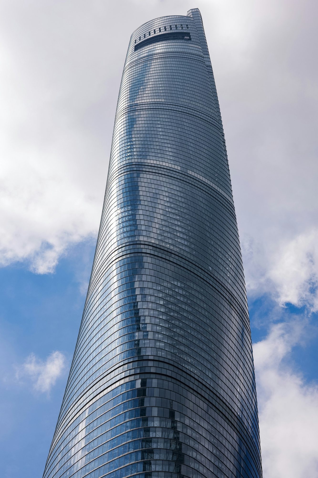 Die gedrehte Glasfassade des Shanghai Tower vor Wolken, vom Fuß bis zur Spitze